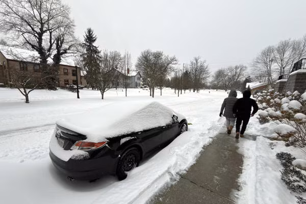 Calles cubiertas de nieve y hielo en una ciudad de Estados Unidos mientras equipos trabajan en la limpieza y vehículos circulan lentamente.
